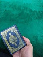 A photo of man hand holding a holy Qur'an with green background for copy space, hand holding a Quran book isolated for copy space