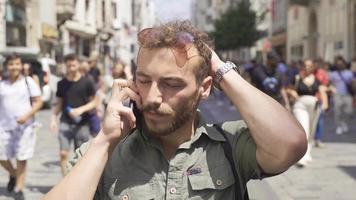 hablando en el teléfono en el concurrido calle. joven hombre obtiene estresado y nervioso mientras hablando en el teléfono. video