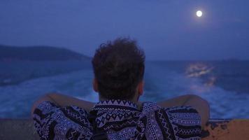 el hombre mirando a el mar y el Luna a noche. Luna y marina a noche en el imagen tomado desde el barco. video