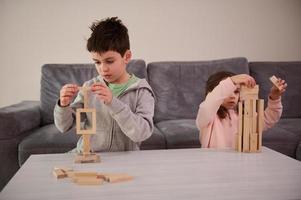 Creative children, brother and sister concentrated on building from wooden blocks, playing developmental board games, building complex tall wooden structures at home. Educational leisure and pastime photo