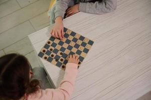Overhead view of children hands placing and arranging checkers pieces on a chessboard. Logic development., intellectual board games, education, concentration and smart leisure concept photo