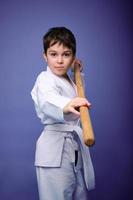 Confident strong concentrated boy - Aikido wrestler - in a kimono stands with a wooden jo weapon in his hands. Oriental martial arts practice concept photo