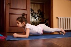 Little girl practicing yoga, doing push ups, press ups, four limbed staff exercise, chaturanga dandasana pose indoors photo