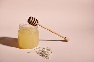 Still Life with wooden dripper on a jar with organic honey and dried bouquet of meadow flowers on pink pastel background photo