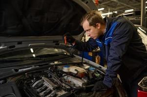 Concentrated Caucasian young man, car engineer technician mechanic in professional uniform, automobile mechanic repairman testing and checking oil level in the car engine. Car service and maintenance photo