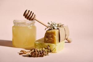 Honey spa concept. Still life. A jar of organic honey and wooden stick, hop cones and bars with natural soap and shampoo photo