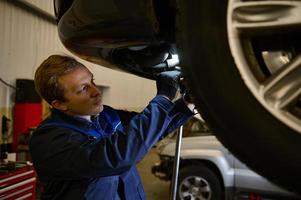 Mechanic checking the alignment of car checking the chassis using a lamp. Car engineer checking tire in maintenance service center. Technician or engineer professional work for customer photo