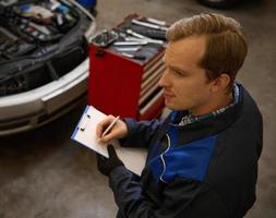 Overhead view of Automobile mechanic repairman checking a car engine with inspecting writing to the clipboard. Mechanical maintenance engineer working in automotive industry. photo