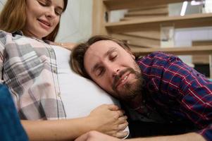 Lovely cute couple, young dad-to-be leaning gently on the belly of his cute pregnant wife, enjoying the expectation of the baby together. Happy and carefree pregnancy and family relationships concept photo