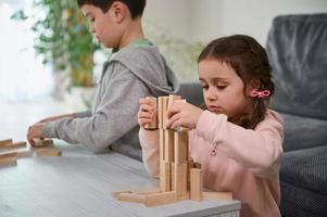 Creative kids, European boy and girl playing with game stacking wooden toy blocks in high building structure. Hand movement control and concentration skills, educational leisure and board game concept photo