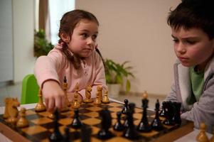 Adorable Caucasian children, two diverse funny kids teenage boy and preschooler girl playing chess at home. Kids intellectual education and entertainment concept, childhood, family relationships photo