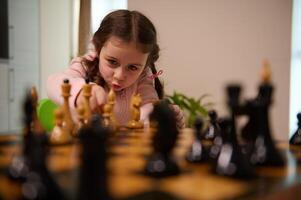 Adorable little girl picking up a chess piece while playing chess game at home. Smart intellectual board games for kids, logic development, education concept photo