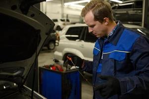 Mechanic in garage checking motor oil level at a car. Car engineer technician in the car repair shop. Automobile maintenance and auto service concept photo