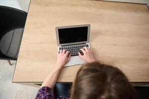 Top view of a business person, businessman, entrepreneur, journalist copywriter freelancer developer working remotely on laptop, typing text on laptop with blank monitor screen with copy ad space. photo