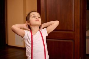 Determined confident Caucasian sporty child girl in sportswear, exercising with elastic fitness band on gym mat. photo