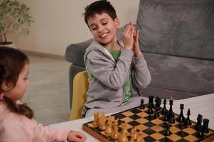 A chess game for a clever mind. Beautiful smart kids having great time, enjoying playing chess together in home interior. The concept of intellectual board games and logic development for kids photo