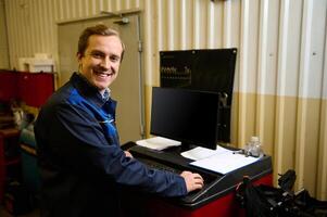 Portrait of a handsome Caucasian man, an auto mechanic, using a PC to diagnose at a car service station. Auto service, car maintenance and repair concept, people and labor concept photo