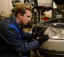 Auto mechanic in car service adjusting headlights on car in the repair shop garage. Auto service, car repair and warranty maintenance concept photo