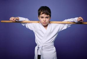 Confident strong European aikido wrestler posing with wooden aikido weapon against violet background with copy ad space. Oriental martial arts practice photo