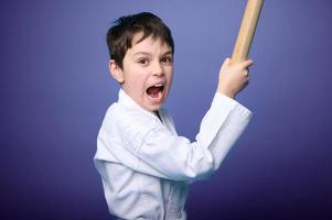 Strong schoolboy - aikido fighter holds bamboo katana weapon and practices martial skills, isolated on purple background with copy ad space photo