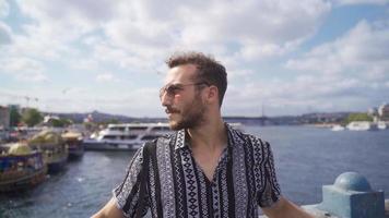 hermoso hombre en Estanbul. joven hombre en Gafas de sol gasto hora por el mar en eminonu cuadrado. video