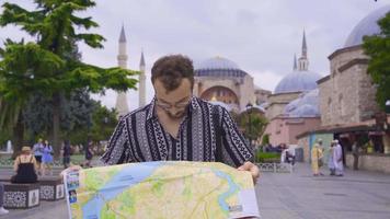 Jeune homme est en marchant autour à la recherche à une papier carte dans le sien main. touristique homme visite Istanbul est en voyageant par à la recherche à le papier carte dans le sien main. video