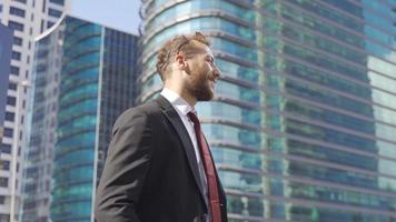 Businessman standing near Company Buildings. Businessman looks at his watch and speaks on the phone. video