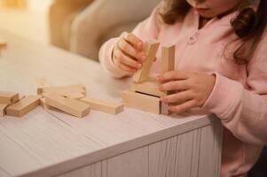 Close-up of baby girl hands building wooden structure with blocks and bricks. Fine motor skills development, educational board games concept with copy ad space photo