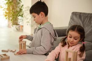 desarrollo de multa motores habilidades y concentración, educativo ocio, familia pasatiempo concepto. enfocado niños edificio estructuras con de madera bloques, jugando tablero juegos en el hogar vivo habitación. foto