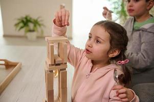 Focus on adorable little preschool girl playing board game with her brother building high wooden block buildings. The concept of the development of fine motor skills. photo