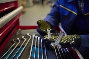 Close-up of the hands in work gloves of a car engineer mechanic holding wrenches above the box with set of mechanic tools for repair and car maintenance photo