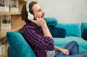 Handsome young Caucasian man enjoying listening music on headphones while sitting on a couch at home and relaxing at his day off photo