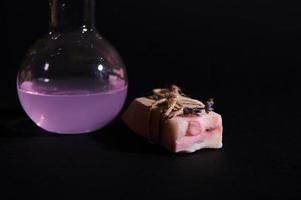 Details on a bar of organic natural soap and lab flask with purple extract of lavender flower, isolated black background photo