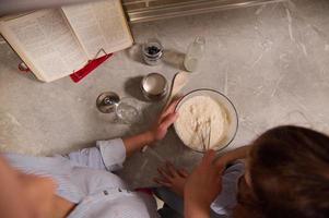 parte superior ver de un bonito mujer, contento amoroso madre y su adorable hija preparando tortita masa, mezcla ingredientes en cuenco con batidor en cocina encimera carnaval martes, alimento, culinario concepto foto