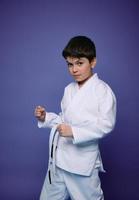 retrato de un hermoso caucásico Adolescente chico, aikido luchador practicando marcial habilidades en contra púrpura pared antecedentes. oriental marcial letras concepto foto