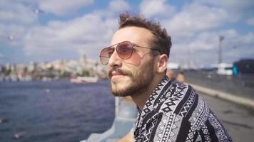 joven hombre mirando a gaviotas por el mar. joven hombre en Gafas de sol soportes en contra el mar y relojes el Gaviotas video