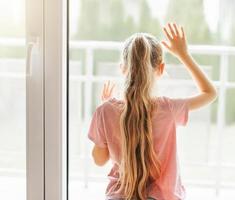 Sad little girl looking through  window at home. photo