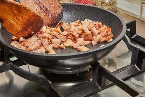 Chopped bacon with onions is fried in pan on gas stove photo