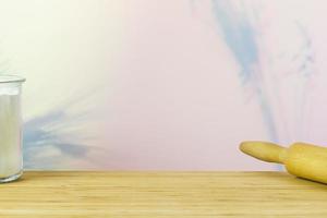 Empty wooden kitchen table with dough roller and glass of flour photo