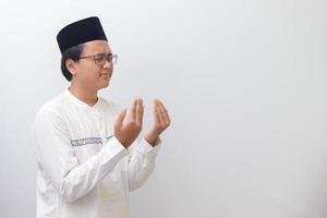 Portrait of young millennial Asian muslim man praying earnestly with his hands raised. Isolated image on white background photo