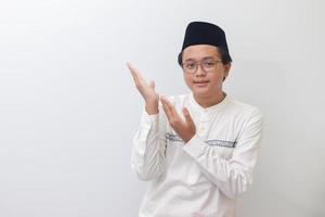 Portrait of young Asian muslim man showing product and pointing with his hand and finger. Isolated image on white background photo