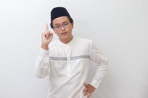 Portrait of young Asian muslim man pointing up his forefinger and reminding something to do. Advertising concept. Isolated image on white background photo