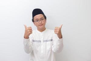 retrato de joven asiático musulmán hombre sonriente y mirando a cámara, haciendo pulgares arriba mano gesto. aislado imagen en blanco antecedentes foto