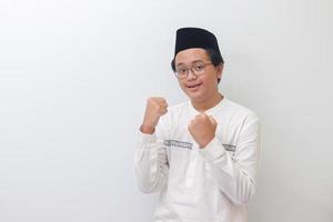 Portrait of young Asian muslim man raising his fist, celebrating success and looking at camera. Isolated image on white background photo