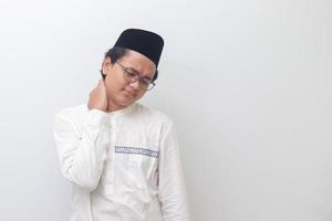 Portrait of young Asian muslim man feeling pain in neck. Isolated image on white background photo