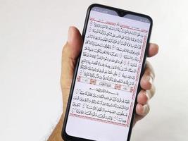 Indonesia, April 2023. Hand holding mobile phone showing quran application at surah al-Kahfi. photo