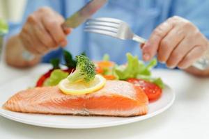 Asian elderly woman patient eating salmon stake and vegetable salad for healthy food in hospital. photo