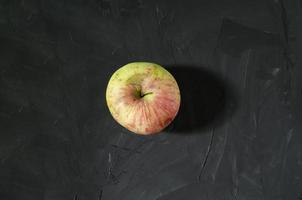 The single apple in the middle of the dark gray background. Red and yellow ripe apple. Concrete background. photo