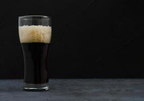 un medio litro de oscuro cerveza con espuma, oscuro antecedentes. foto