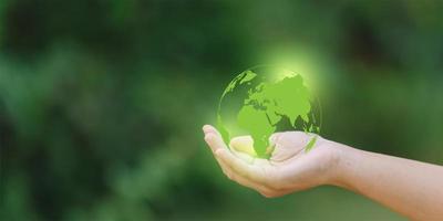 Human hand holding a green earth globe on blurred nature background, save the world concept photo